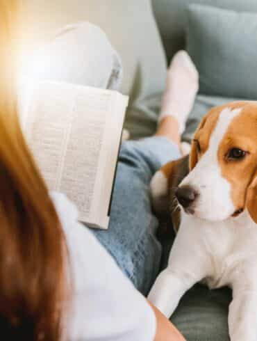 woman reading a book while dog lays on her lap