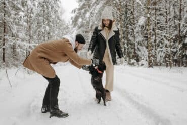 pet parents playing with their black dog in the snow